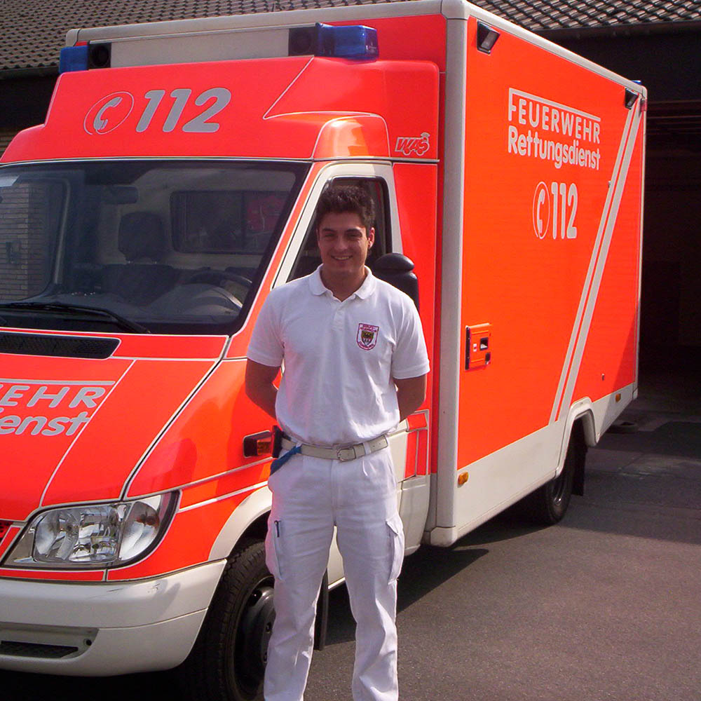 Feuerwehrmann und Gründer Enrico steht als Notfallsanitäter vor einem Rettungswagen